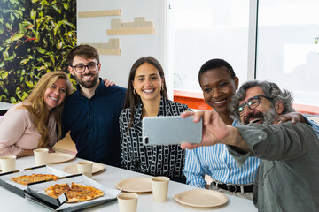 Multi-ethnic group of business co-workers taking selfie and having fun on lunch break in the office.