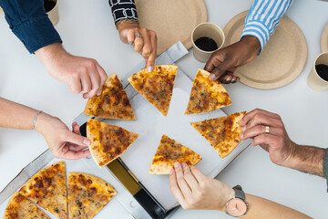 Close-up of a hands taking slices of pizza on a lunch break.