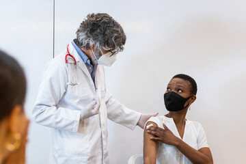 Male nurse with mask giving vaccine to patient in clinic.
