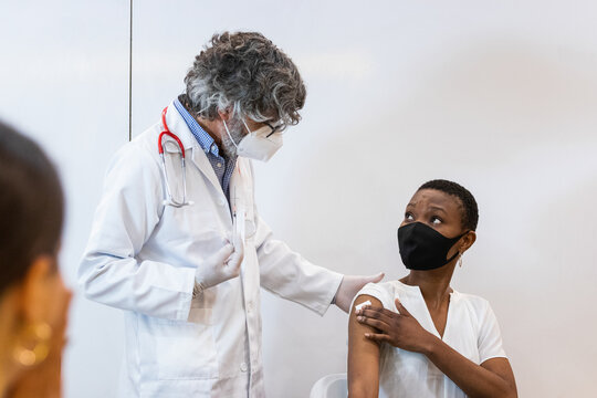 Male Nurse With Mask Giving Vaccine To Patient In Clinic.