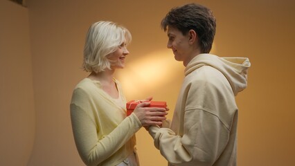 Young attractive man giving his beautiful girlfriend gift in red box, sharing their happiness 