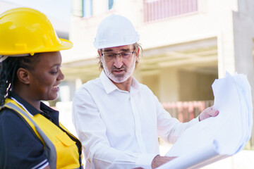 Female black ethnicity engineer taking to caucasian white client about the construction plan in blue print.