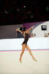Rhythmic gymnastics in the professional arena. Performance with colored maces in front of the audience and judges
