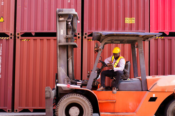 African black ethnicity sitting on a forklift vehicle and working on a digital tablet at container shipyard. 