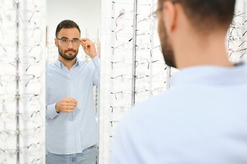 Young man choosing spectacles at optic shop