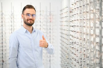 Young man choosing spectacles at optic shop