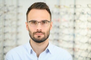 Young man choosing spectacles at optic shop