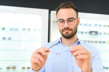 Young man choosing spectacles at optic shop