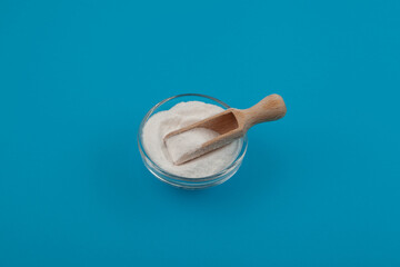 Succinic acid powder on blue background. Butanedioic acid or spirit of amber. Food additive E363, used as flavoring agent, contributing a somewhat sour and astringent component to umami taste