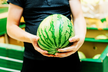 Hand is holding watermelon from supermarket shelf, close up photo