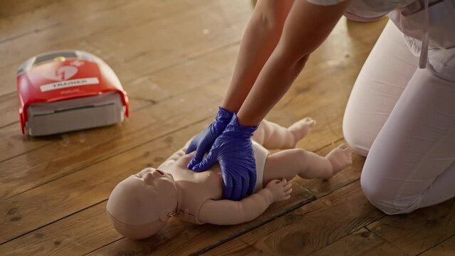 Close up shooting: A professional nurse in a white medical uniform teaches a group of people first aid and demonstrates cardiopulmonary resuscitation techniques using a baby dummy. Medical training