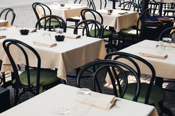 Outdoor empty coffee and restaurant terrace with white tables, vintage chairs and glasses in Europe. Cafe terrace on the pedestrian street in Padua, Italy. A set table is waiting for customers.