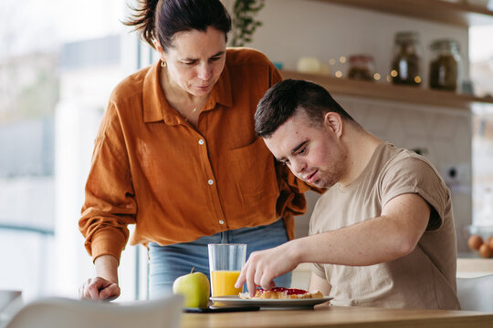 Young man with Down syndrome preparing breakfast with his mother at home. Morning routine for man with Down syndrome.