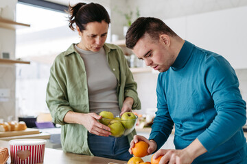 Fototapeta premium Young man with Down syndrome preparing breakfast with his mother at home. Morning routine for man with Down syndrome.