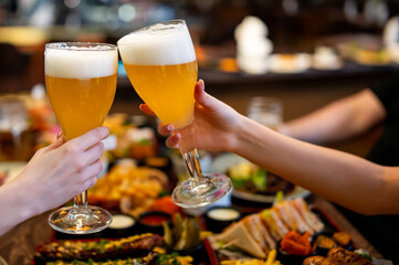 Two friends woman hands clinking glasses of craft beer at the pub or bar