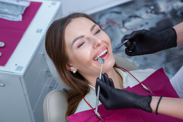 Closeup of female patient showing her beautiful white teeth while having treatment at dental clinic, dentist hands in rubber gloves holding dental tools