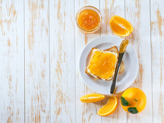 Toast bread with homemade orange jam on a white wooden table served with fresh orange  in side view with copy space for breakfast or brunch.