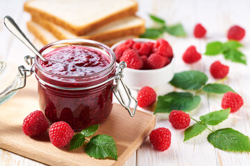 Jar of tasty raspberry jam on a white wooden table. Slices of bread with raspberry jam for breakfast .