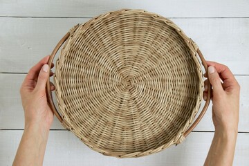 Top view of female hands holding empty round wicker tray with wooden handles. Mock-up for design,...