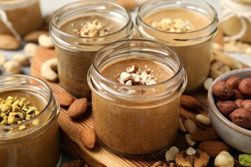 Tasty nut butters in jars and raw nuts on table, closeup