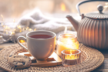 Cozy home composition with a cup of tea, candles and a teapot.