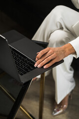 A business woman in a white suit works at a laptop in the office and drinks coffee. Office work concept. Remote work on a PC