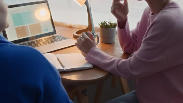 Cropped shot of two deaf and mute female university students doing home assignment together, sitting at desk in front of laptop and communicating with help of sign language