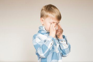 Little boy drinks water from a glass on a gray background in the studio