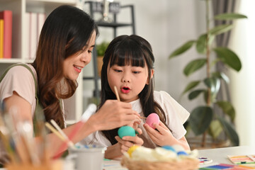 Fototapeta premium Little girl child girl and her mother painting Easter egg with colorful paints at home