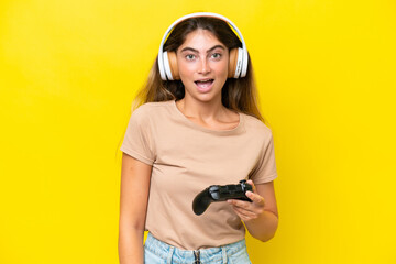 Young caucasian woman playing with a video game controller isolated on yellow background with...