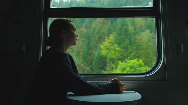 Happy woman in the train. Female traveler staring at mountains through train window and enjoying nature landscape
