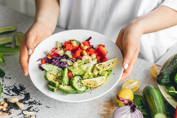 A plate with chopped fresh vegetables in female hands in the kitchen.