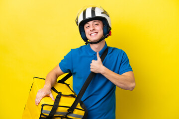 Young Brazilian man with thermal backpack isolated on yellow background giving a thumbs up gesture