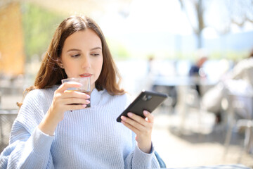 Woman drinking soda in a bar terrace checking phone