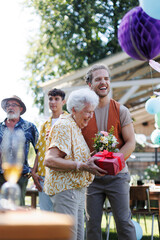 Garden birthday party for senior lady. Beautiful senior birthday woman receiving birthday gift from grandson.