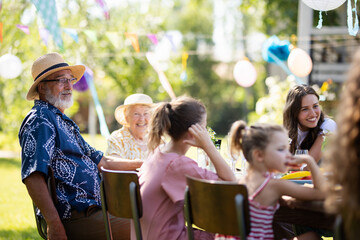 Family chatting, and having fun at party table during summer garden party. Grandfather sitting at...