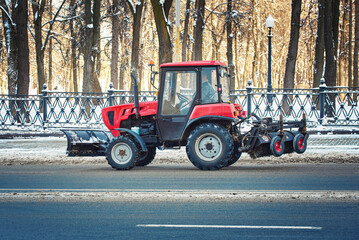 Tractor with snow plow and brush driving on snowy road. Road maintenance in winter season, cleaning...