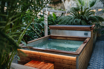 Wooden hot tub among the greenery, houseplants, in hotel greenhouse. Wellness weekend in spa.