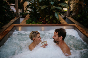 Beautiful mature couple relaxing in hot tub, drinking champagne, enjoying romantic wellness weekend...