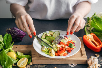 A woman eats a vegetarian salad of fresh vegetables, close-up of the plate.