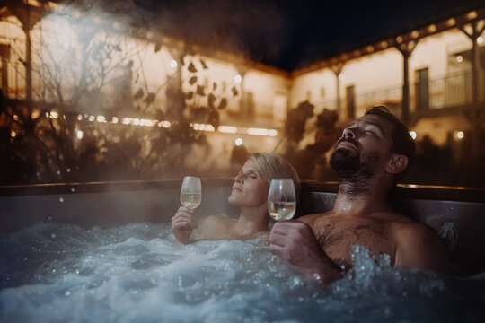 Beautiful Mature Couple Relaxing In Outdoor Hot Tub, Drinking Champagne, Enjoying Romantic Wellness Weekend In Spa. Concept Of Valentine's Day.