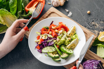 A woman eats a vegetarian salad of fresh vegetables, close-up of the plate.