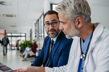 Pharmaceutical sales representative presenting new medication to doctor in medical building,...