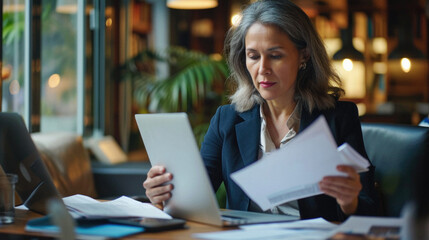 Mature businesswoman working with papers and tablet computer in cafe .