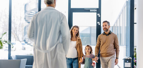 Girl patient looking forward to her doctor and examination in a modern clinic. Girl arriving in hospital with her parents. Emotional support during medical examination.