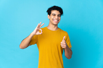 Young Venezuelan man isolated on blue background showing ok sign and thumb up gesture