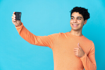 Venezuelan man isolated on blue background making a selfie with mobile phone