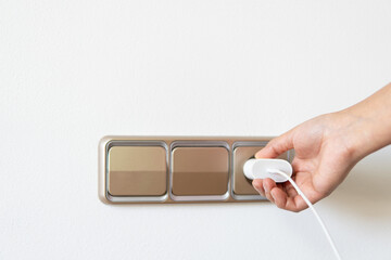 woman's hand plugging a charger into a european peach fuzz plug, white copy space always plugged in