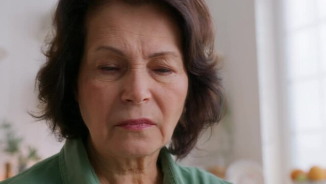 close up view of elderly woman holding pill in hands, frowning. takes medicine and drink water. feels hurting pain and looks suffering. Old pensioner dislike nasty taste of medication
