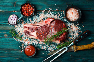 Raw Beef Aged Steak on the Bone with Rosemary, Sea Salt and Spices. On a blue wooden background....